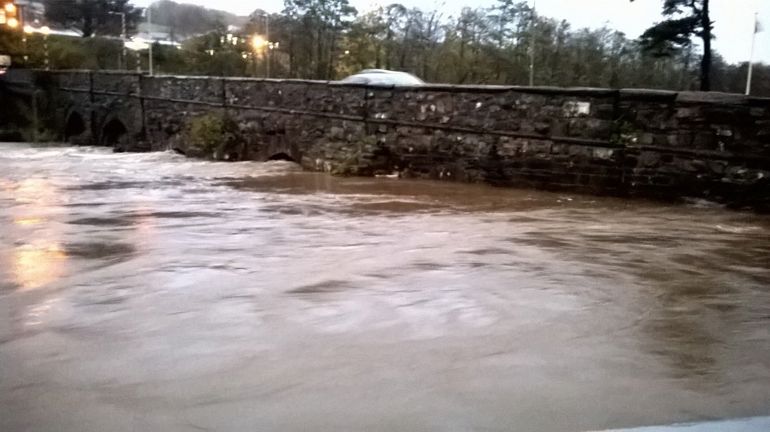 Fast flowing high river against an old brick bridge