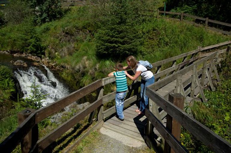Mother and child watching the waterfall from a bridge
