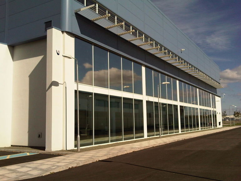 Long building with floor to ceiling glass windows and a grey roof