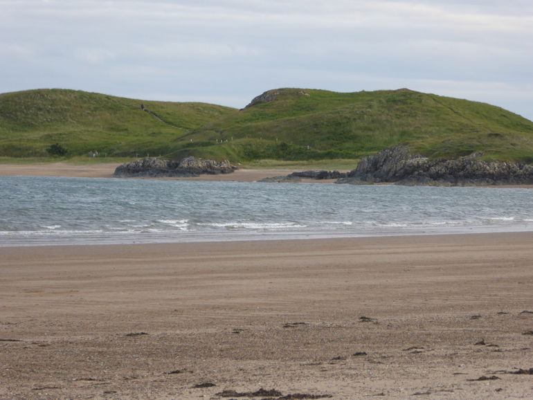 Llun yn dangos tirlun werdd Ynys Llanddwyn o draeth Niwbwrch