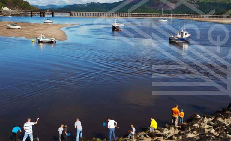 People fishing on an estuary with boats on the water