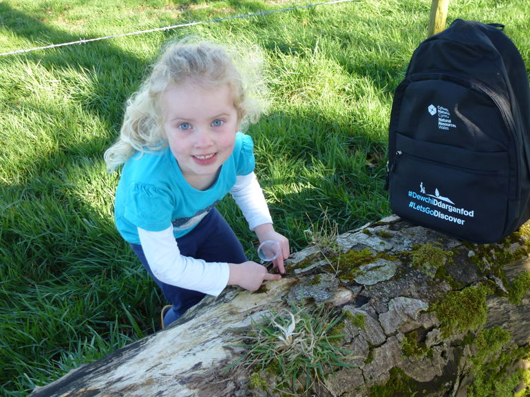 Little girl using a bug pot to collect insects next to a discovery backpack