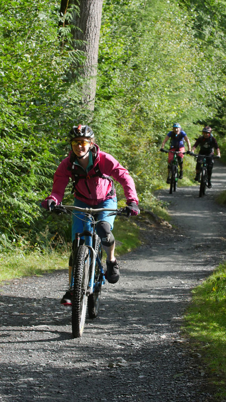 Image of a woman mountain biking with two cyclists in the background