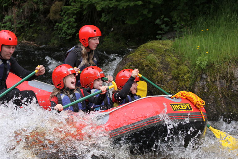 Children and adults paddling in a boat down rapids