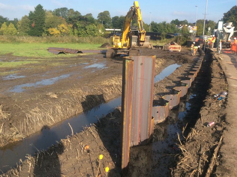 Digger in a muddy field building a steal flood defence