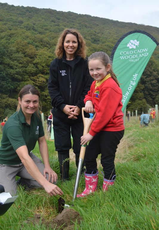 Rebecca Good (Woodland Trust), Kate Thomson (NRW) and a school girl planting a tree
