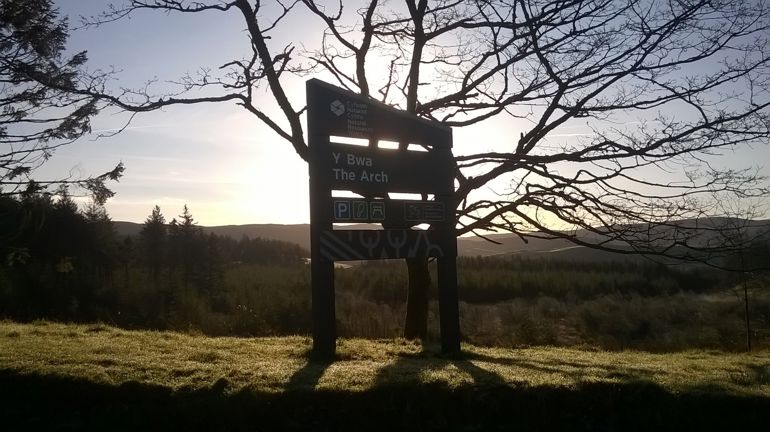 The arch visitor centre sign with the sun setting in the background behind a silhouette of a tree