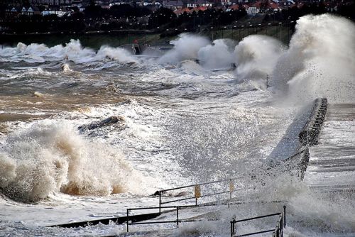 Coastal storm surge at Colwyn Bay with coastal defences visible.